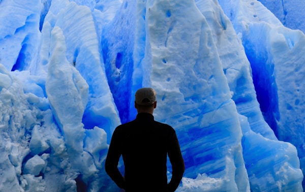 Tony, de dos, devant un glacier.